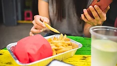 person holding phone while eating fries at foodservice establishment