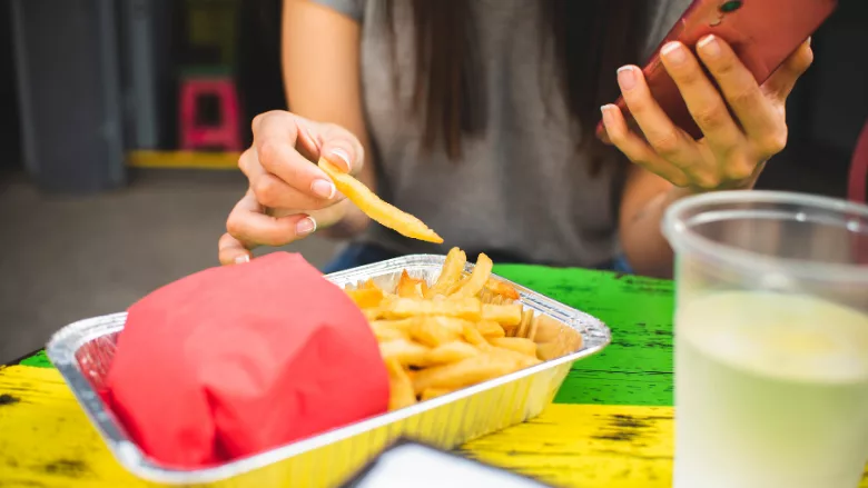 person holding phone while eating fries at foodservice establishment