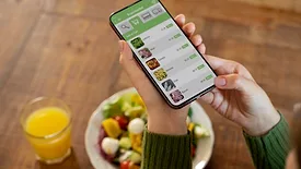 person eating a meal and holding a smartphone displaying online food ordering service