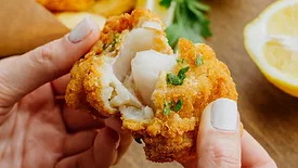 person pulling apart breaded fried white fish