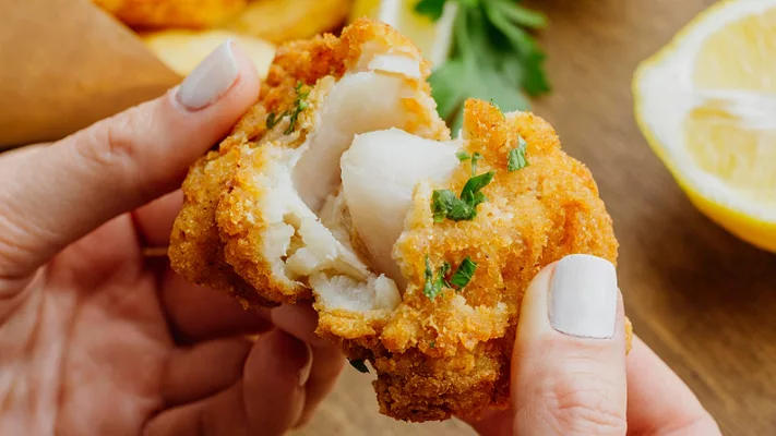 person pulling apart breaded fried white fish