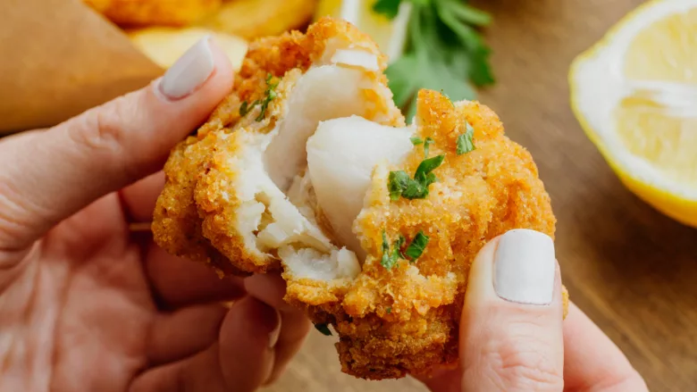 person pulling apart breaded fried white fish