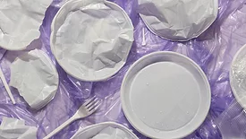 plastic utensils and plates on crumpled plastic film against purple background