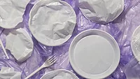 plastic utensils plates on purple background_freepik via magnific.png plastic utensils and plates on crumpled plastic film against purple background