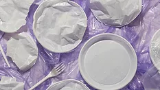 plastic utensils and plates on crumpled plastic film against purple background