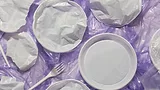 plastic utensils and plates on crumpled plastic film against purple background