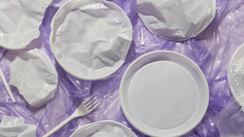 plastic utensils and plates on crumpled plastic film against purple background
