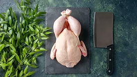 raw whole chicken on cutting board with butcher knife and herb