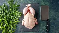 raw whole chicken on cutting board with butcher knife and herb