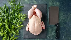 raw whole chicken on cutting board with butcher knife and herb