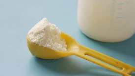 scoop of powdered infant formula in front of bottle against blue backdrop