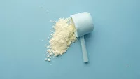 scoop of white powder supplement on blue background