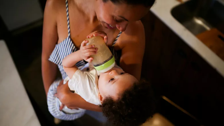 smiling mom feeding baby a bottle in her arms
