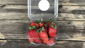 strawberries in a plastic carton that is open on a wooden table