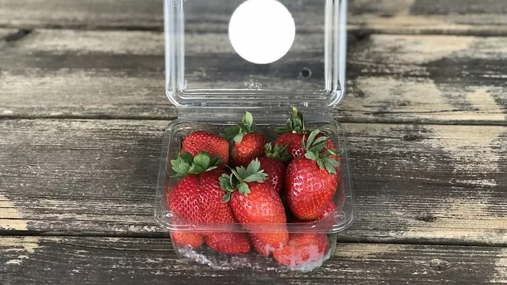 strawberries in a plastic carton that is open on a wooden table