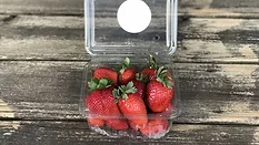 strawberries in a plastic carton that is open on a wooden table