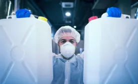 man in PPE holding two jugs of commercial disinfectant