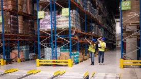 warehouse workers examining pallets of goods on shelves in large storeroom