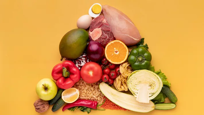 variety of foods arranged in a pyramid shape on yellow background_freepik.png a variety of whole foods including vegetables, meats, nuts, bread, and pasta arranged in a pyramid shape laid against a yellow backdrop