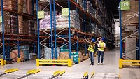 warehouse workers examining pallets of goods on shelves in large storeroom