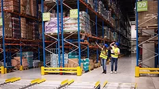 warehouse workers examining pallets of goods on shelves in large storeroom