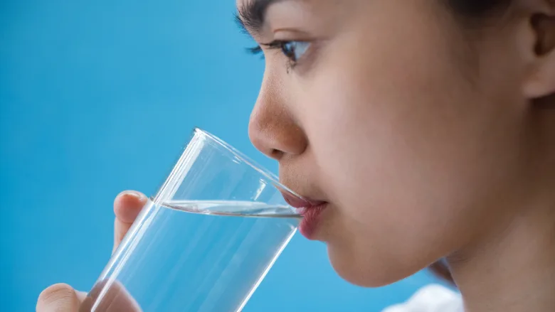 woman drinking glass of water blue background