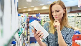 woman looking at box of packaged food in grocery store seeming pensive