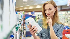 woman looking at box of packaged food in grocery store seeming pensive