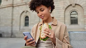 woman scrolling phone and eating sandwich