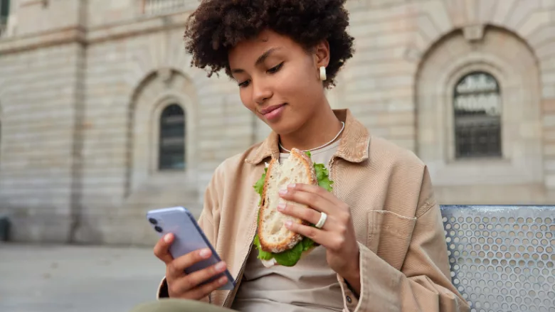 woman scrolling phone and eating sandwich