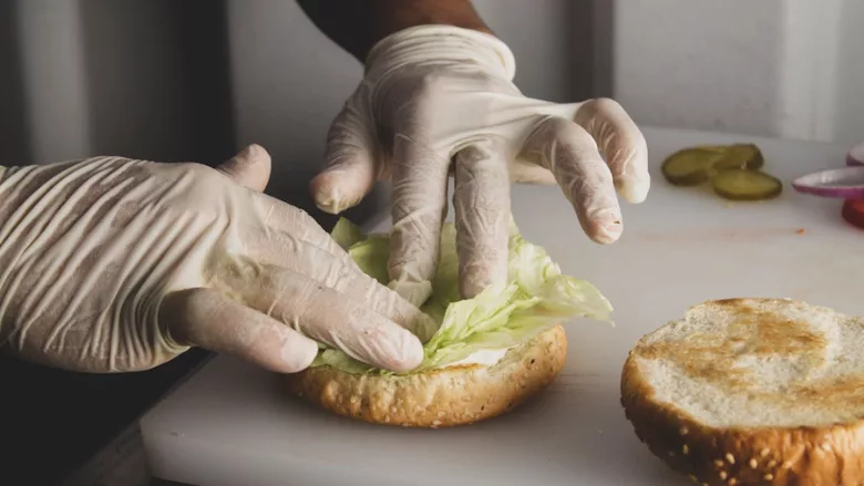 gloved hands of a foodservice worker assembling a burger