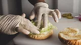 gloved hands of a foodservice worker assembling a burger
