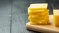 slices off a block of cheddar cheese on a wooden cutting board