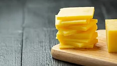 slices off a block of cheddar cheese on a wooden cutting board