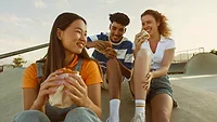 three people smiling and eating food outside