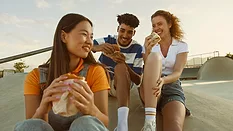three people smiling and eating food outside