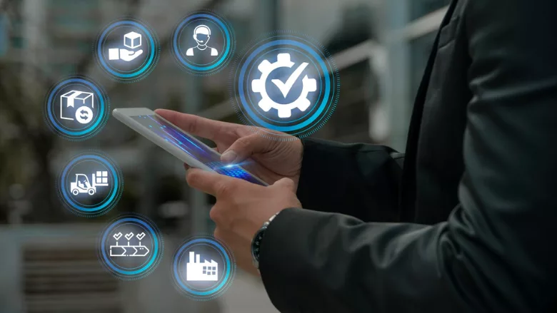 businessman in warehouse holding tablet with digitalized icons hovering around it representing different aspects of supply chain