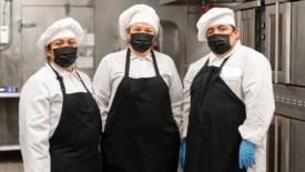 group of chefs in industrial kitchen smiling at camera