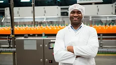 smiling employee in bottling factory looking at camera with arms crossed in front of production line