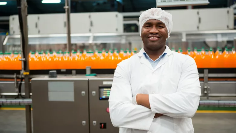smiling employee in bottling factory looking at camera with arms crossed in front of production line