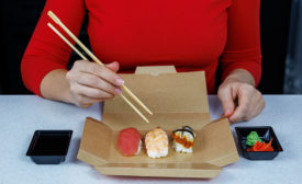 person eating sushi off brown paperboard container